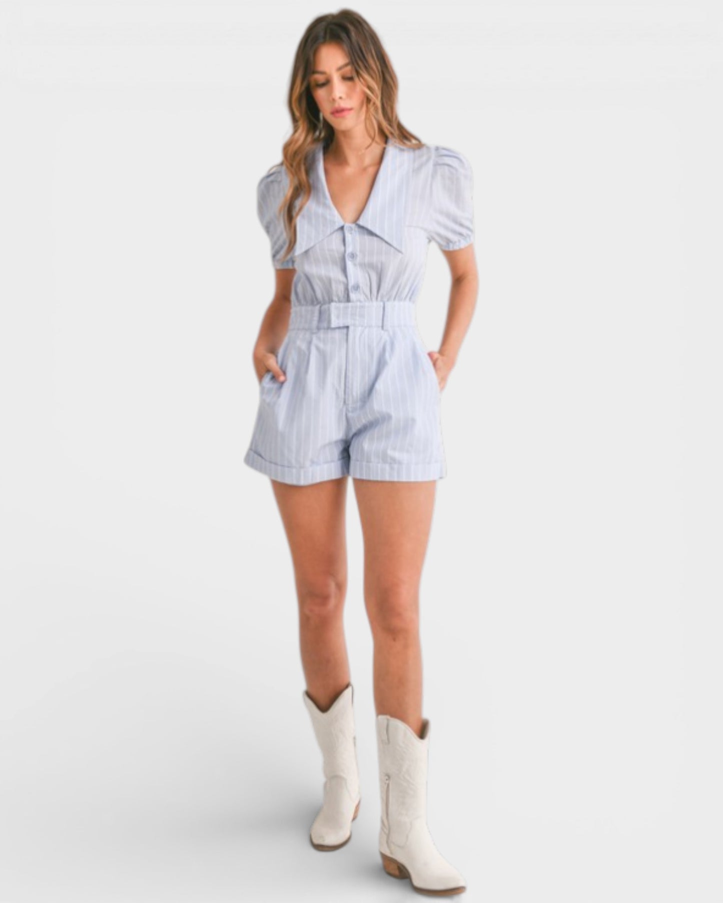 Woman wearing a light blue striped romper with white cowboy boots on a white background