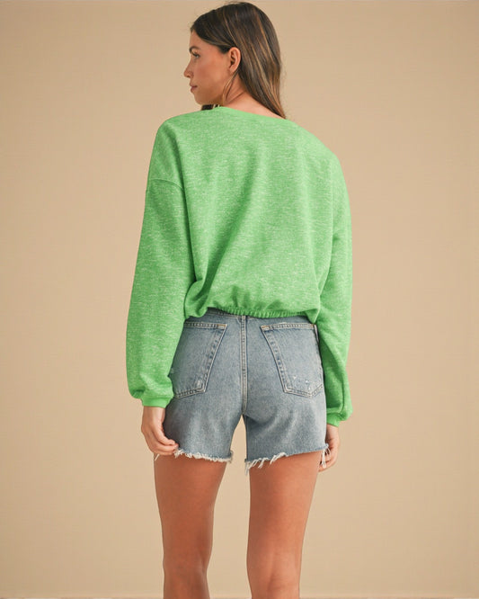 Person wearing a green sweater and denim shorts on a beige background