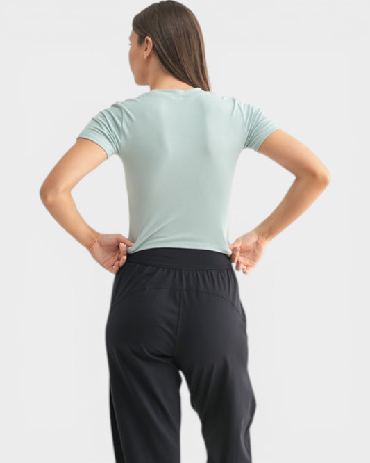 Person wearing a light green t-shirt and black pants on a white background