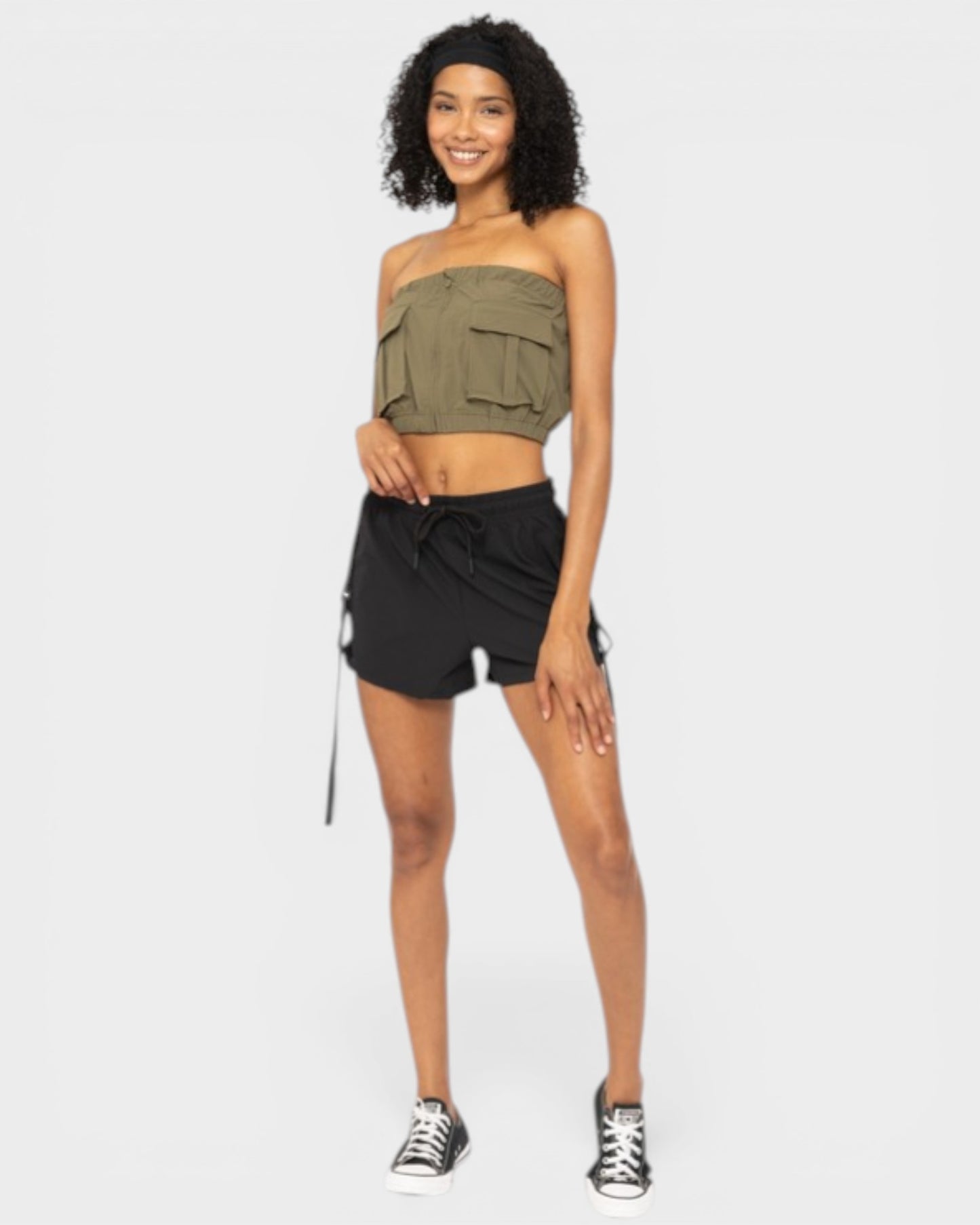 Woman wearing an olive green strapless top and black shorts on a white background