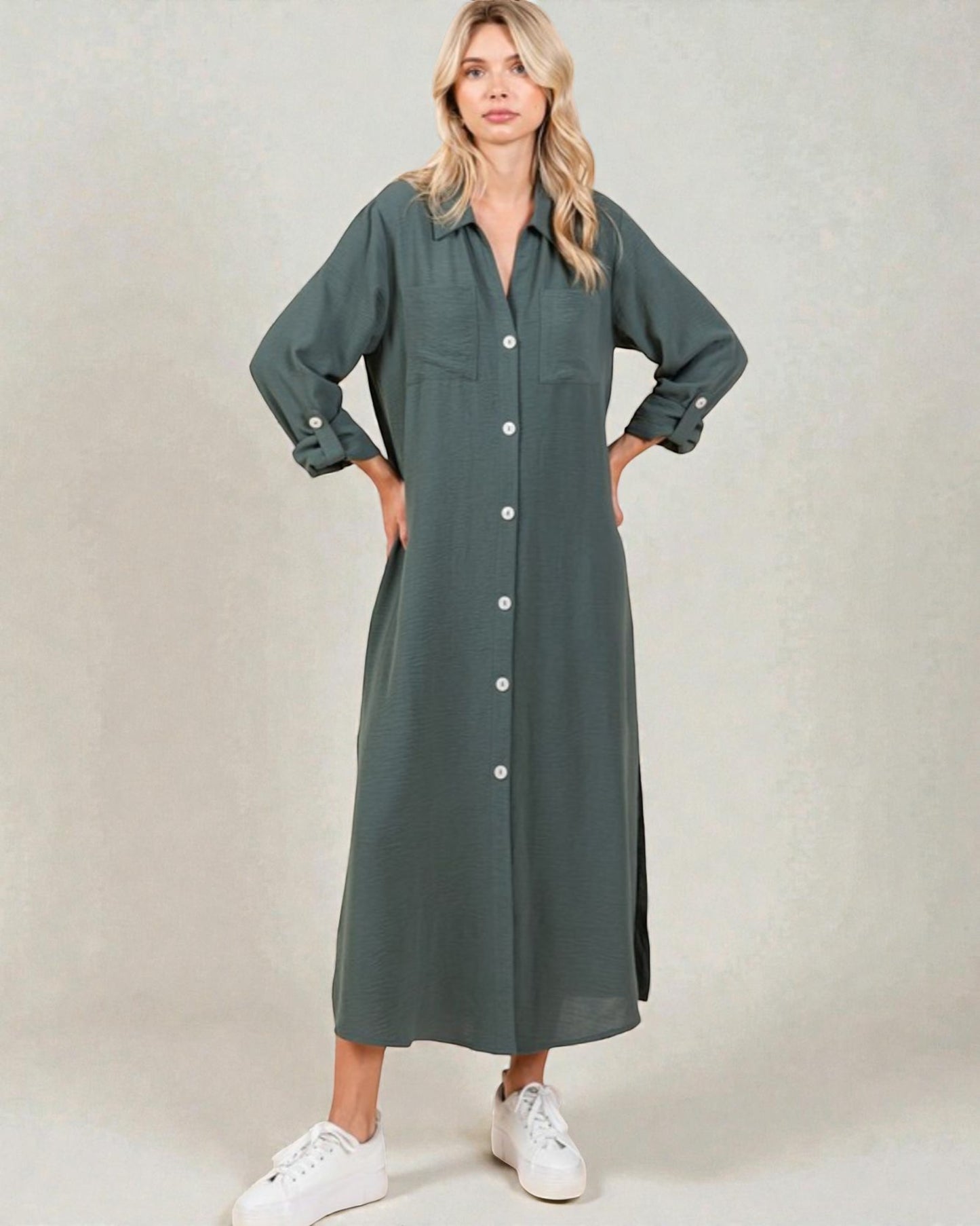 Woman wearing a long green dress with white sneakers on a plain background