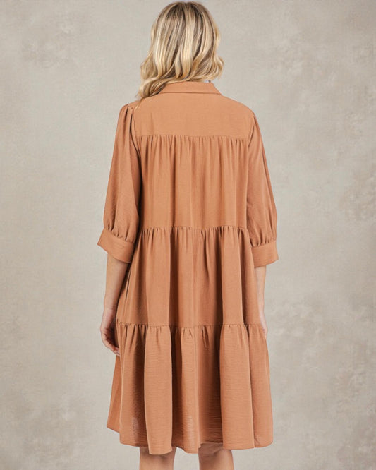 Woman wearing a brown tiered dress against a plain background