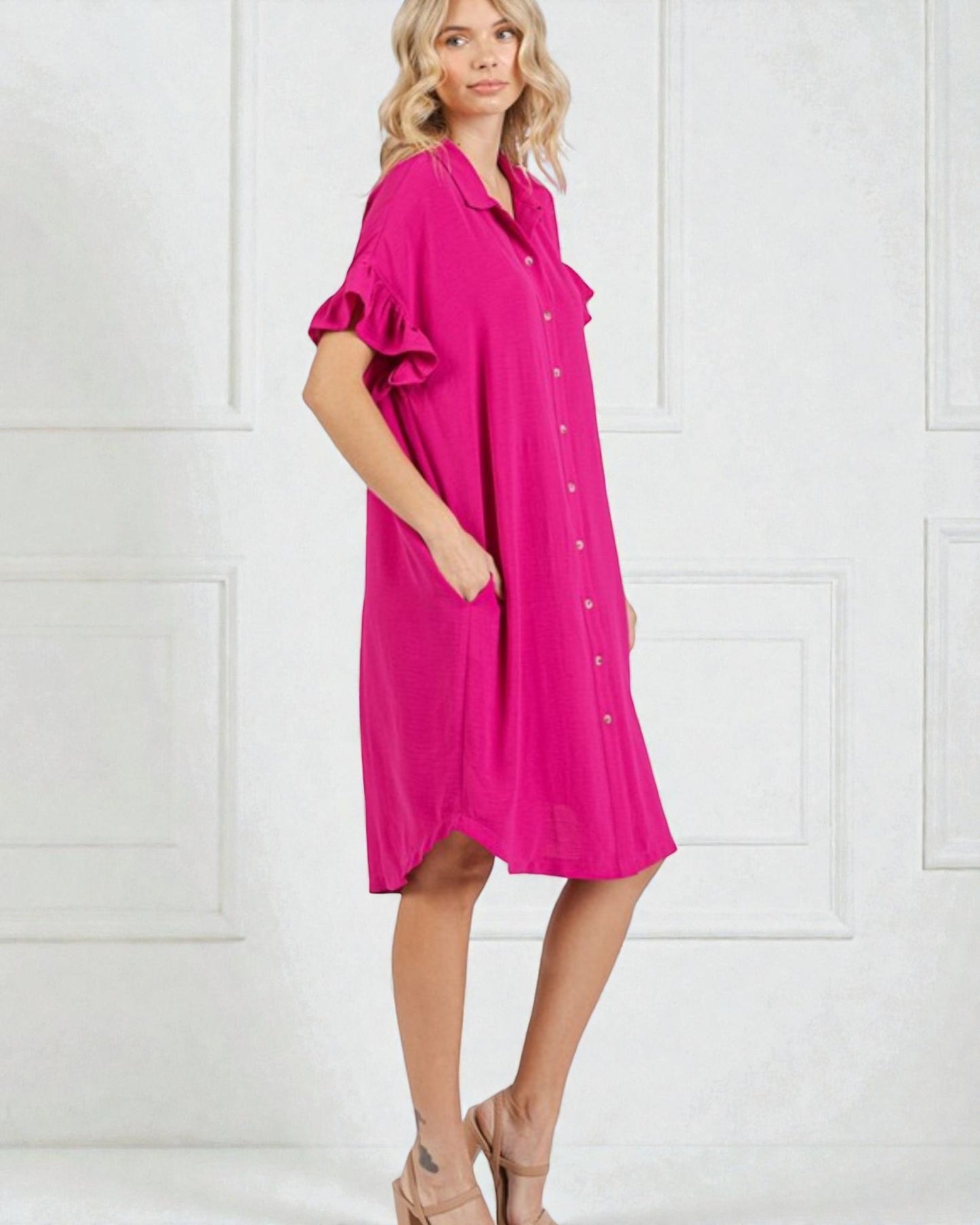 Woman wearing a bright pink dress with ruffled sleeves against a white background