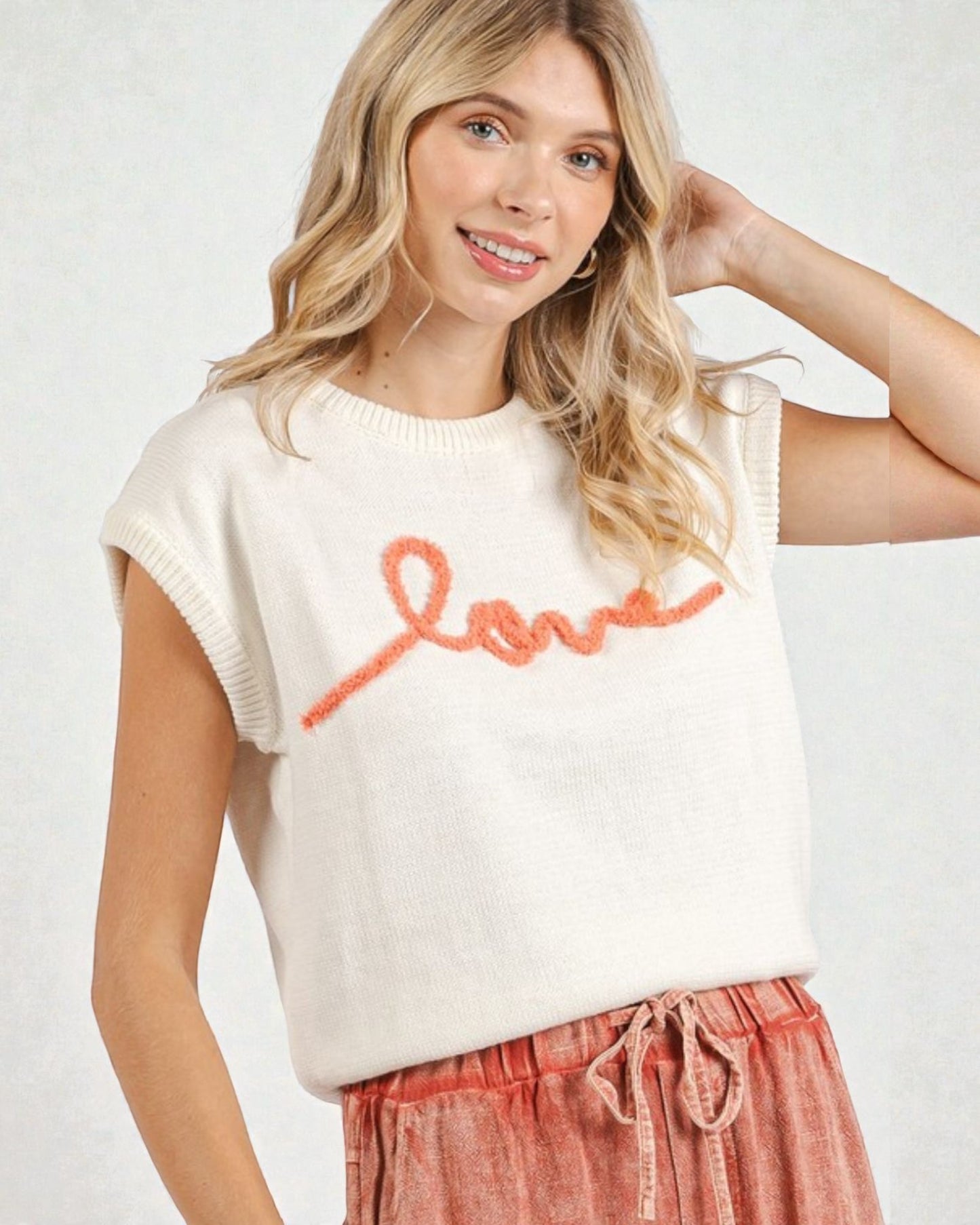 Woman wearing a white sweater with 'love' in red text and pink pants on a white background