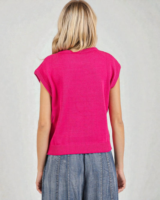 Person wearing a bright pink sleeveless sweater and blue jeans on a plain background