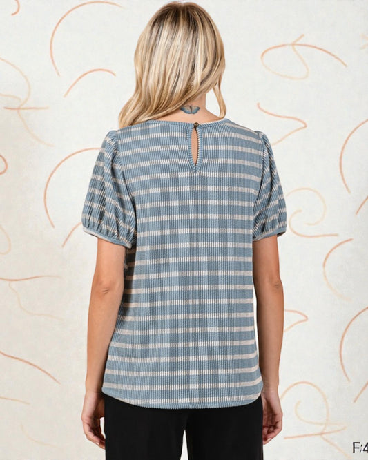 Woman wearing a blue and white striped shirt with puff sleeves against a decorative wall.