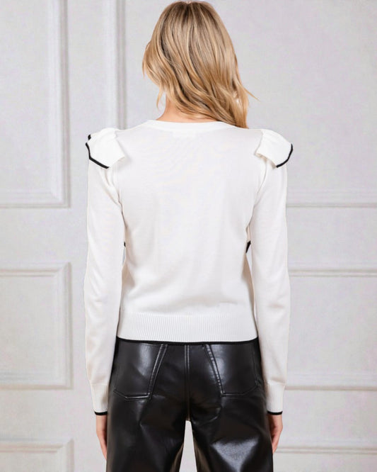 Person wearing a white blouse with black trim and black leather pants against a light-colored wall.
