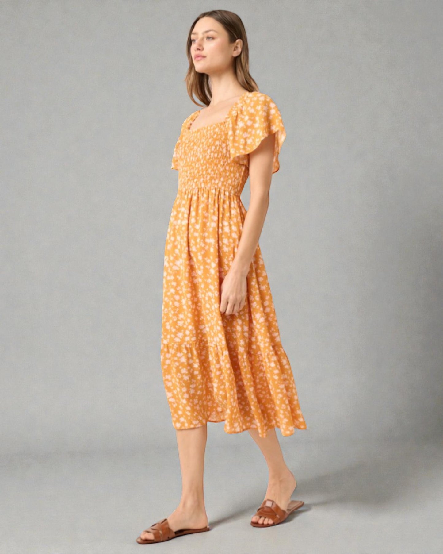 Woman wearing a yellow floral dress against a gray background