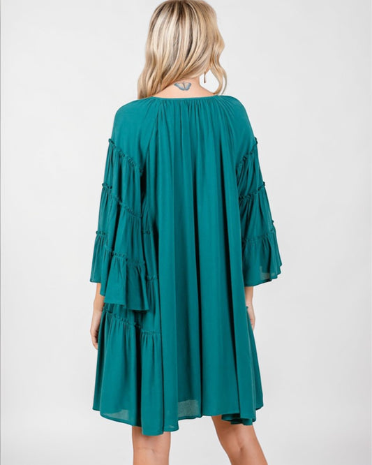 Teal dress with ruffled sleeves and layers worn by a person on a white background