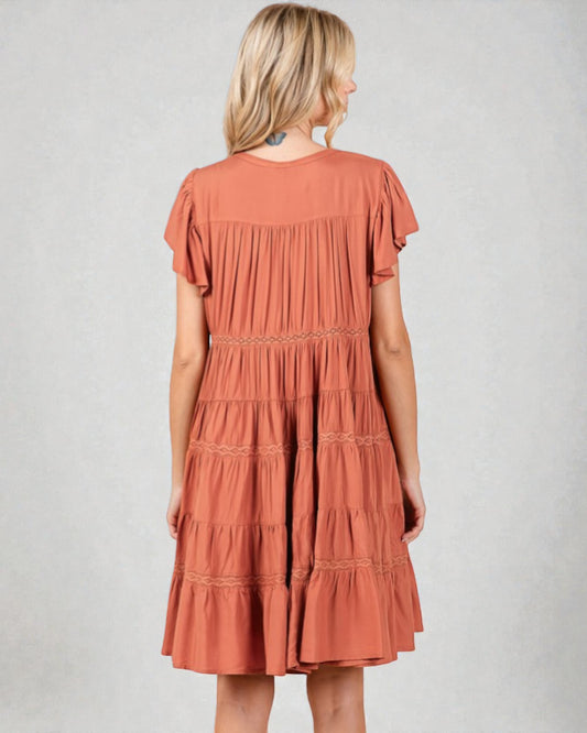 Woman wearing a tiered rust-colored dress on a plain background