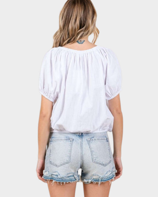 Person wearing a white blouse and denim shorts on a plain background