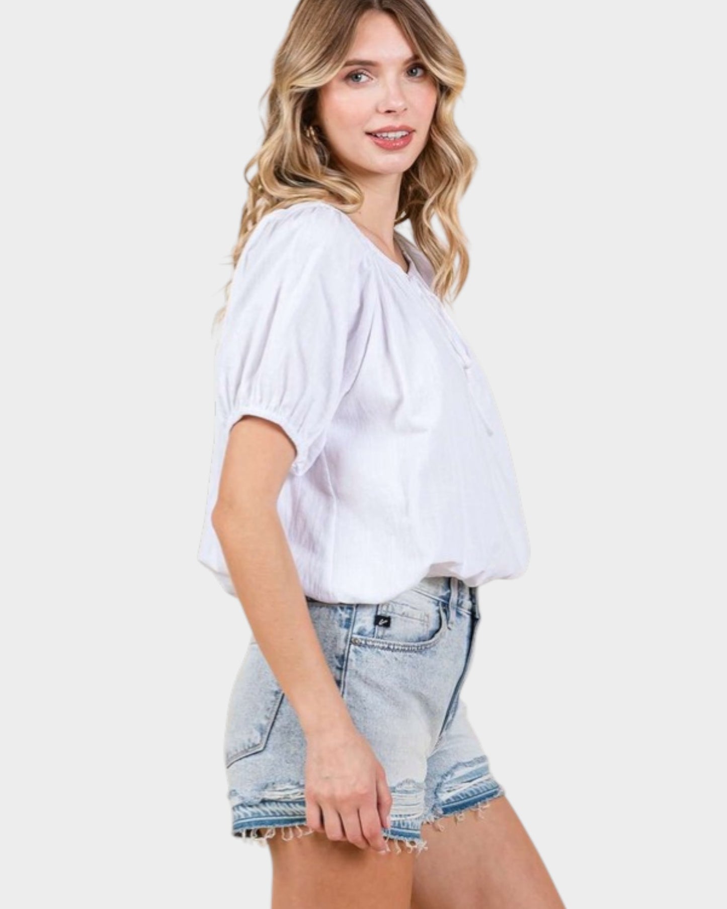 Woman wearing a white blouse and denim shorts on a plain background