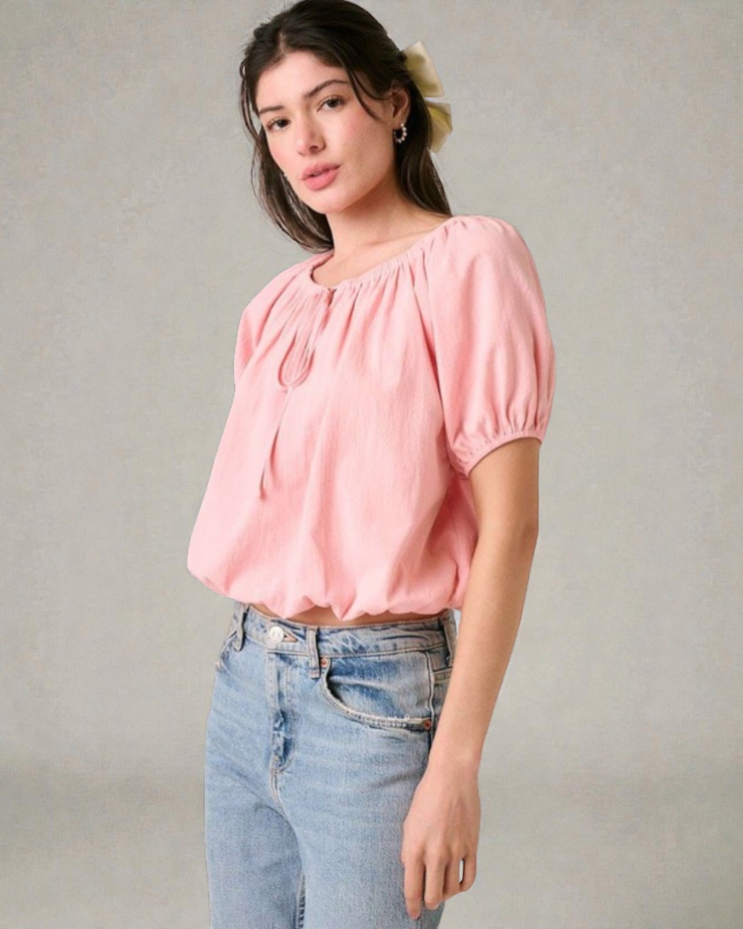 Woman wearing a pink blouse and blue jeans against a plain background
