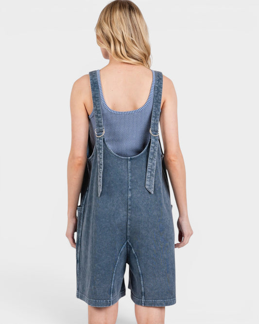 Person wearing a blue denim overall dress on a white background