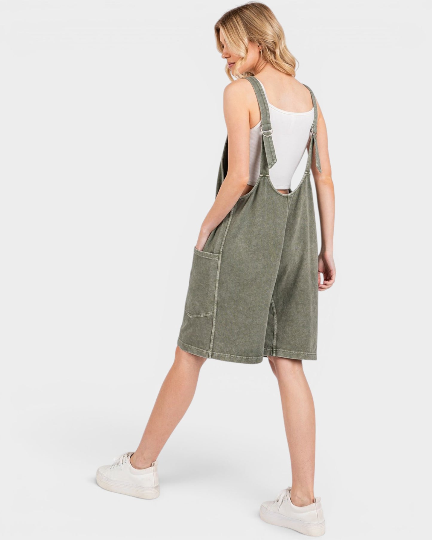 Person wearing a green denim pinafore dress on a white background