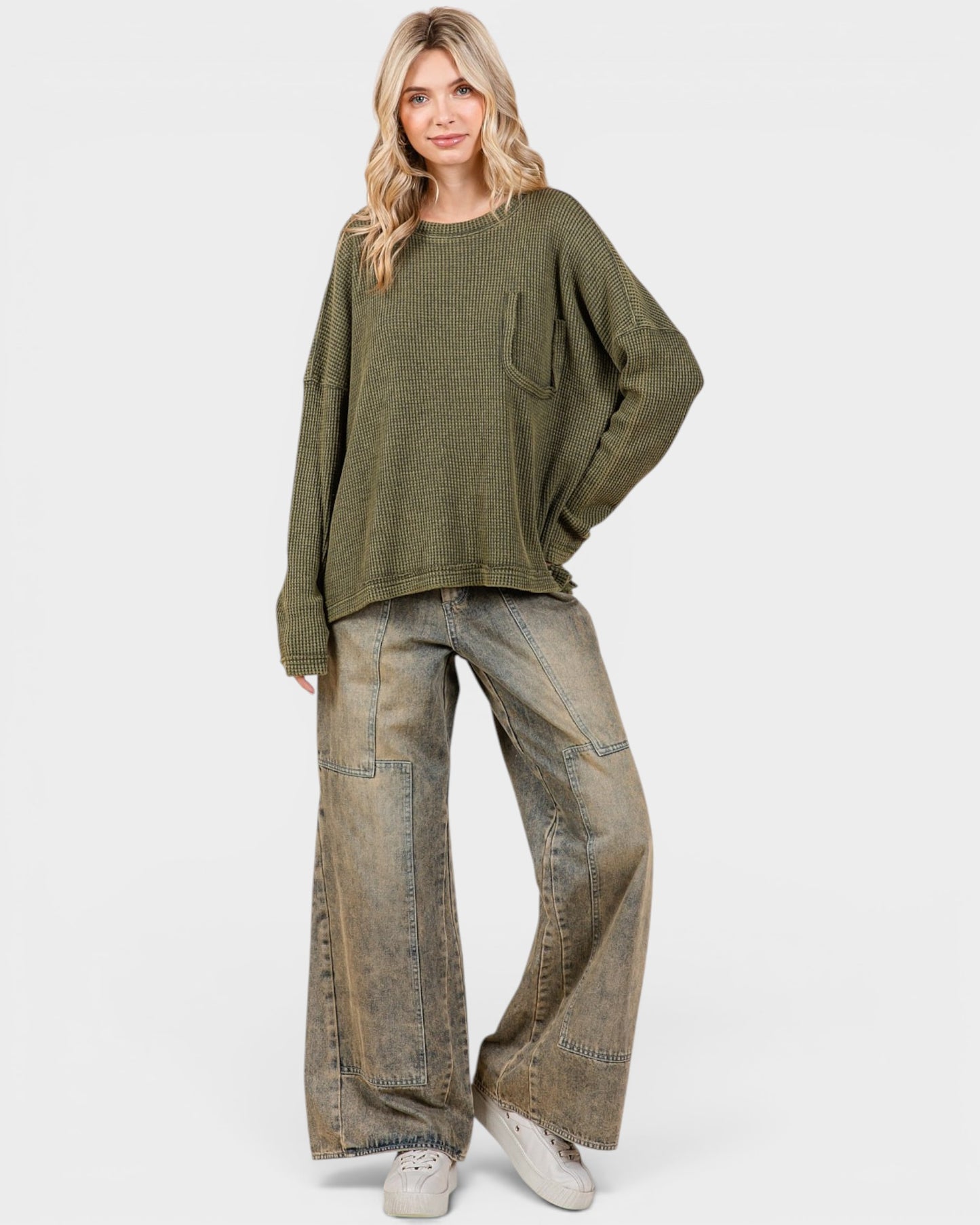 Woman wearing a green sweater and wide-leg jeans on a white background