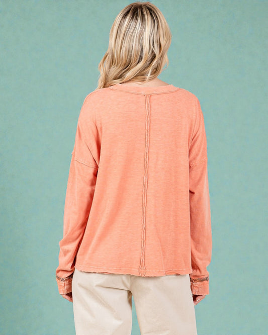 Person wearing a coral long-sleeve top against a teal background