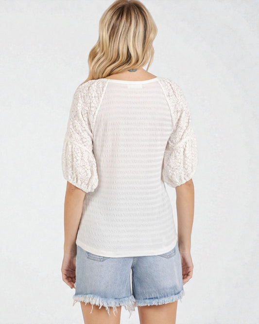 Woman wearing a white lace top and denim shorts on a plain background