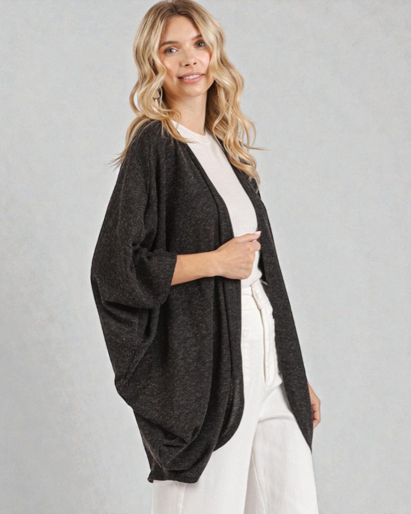 Woman wearing a dark gray cardigan over a white top and pants on a light gray background