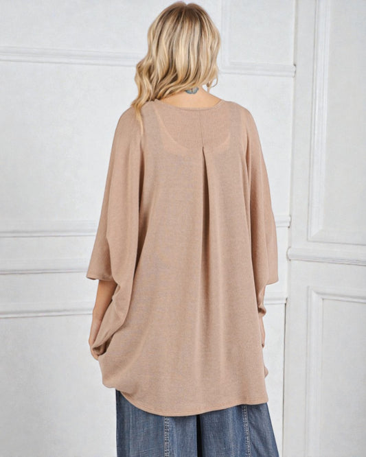 Person wearing a beige oversized sweater against a white wall