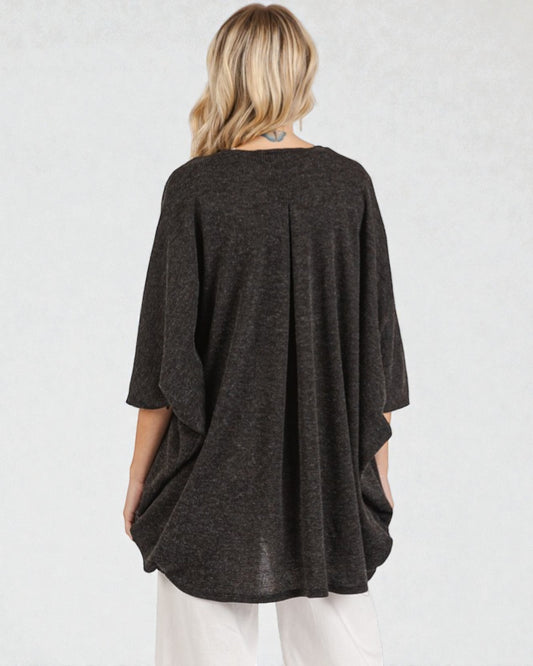 Person wearing a dark gray poncho over a white outfit on a light gray background