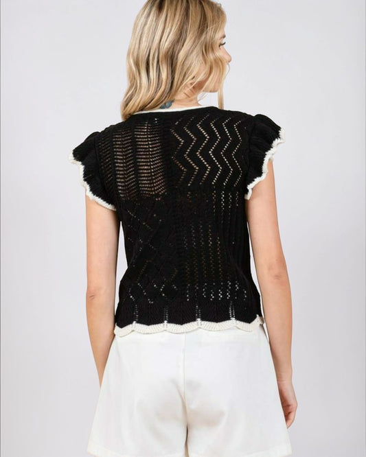 Woman wearing a black knitted top with white trim on a plain background