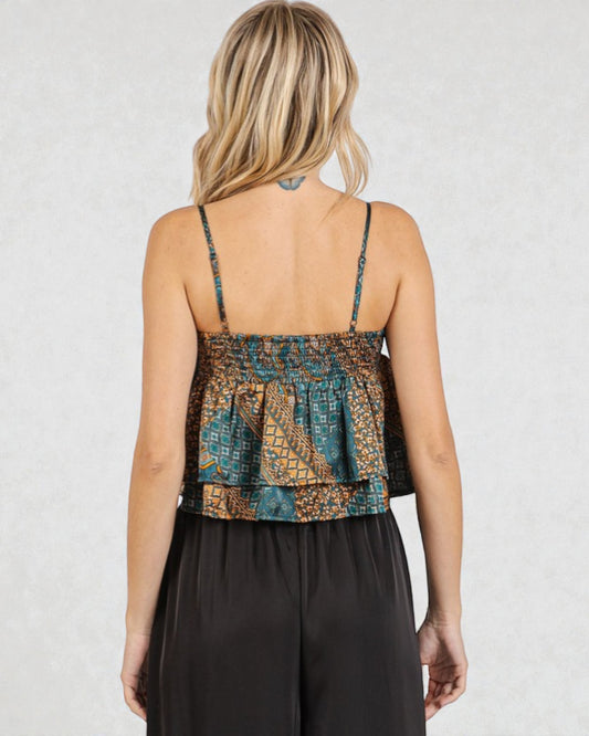 Woman wearing a patterned top and black pants on a plain background