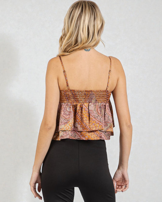 Woman wearing a patterned top and black pants on a plain background