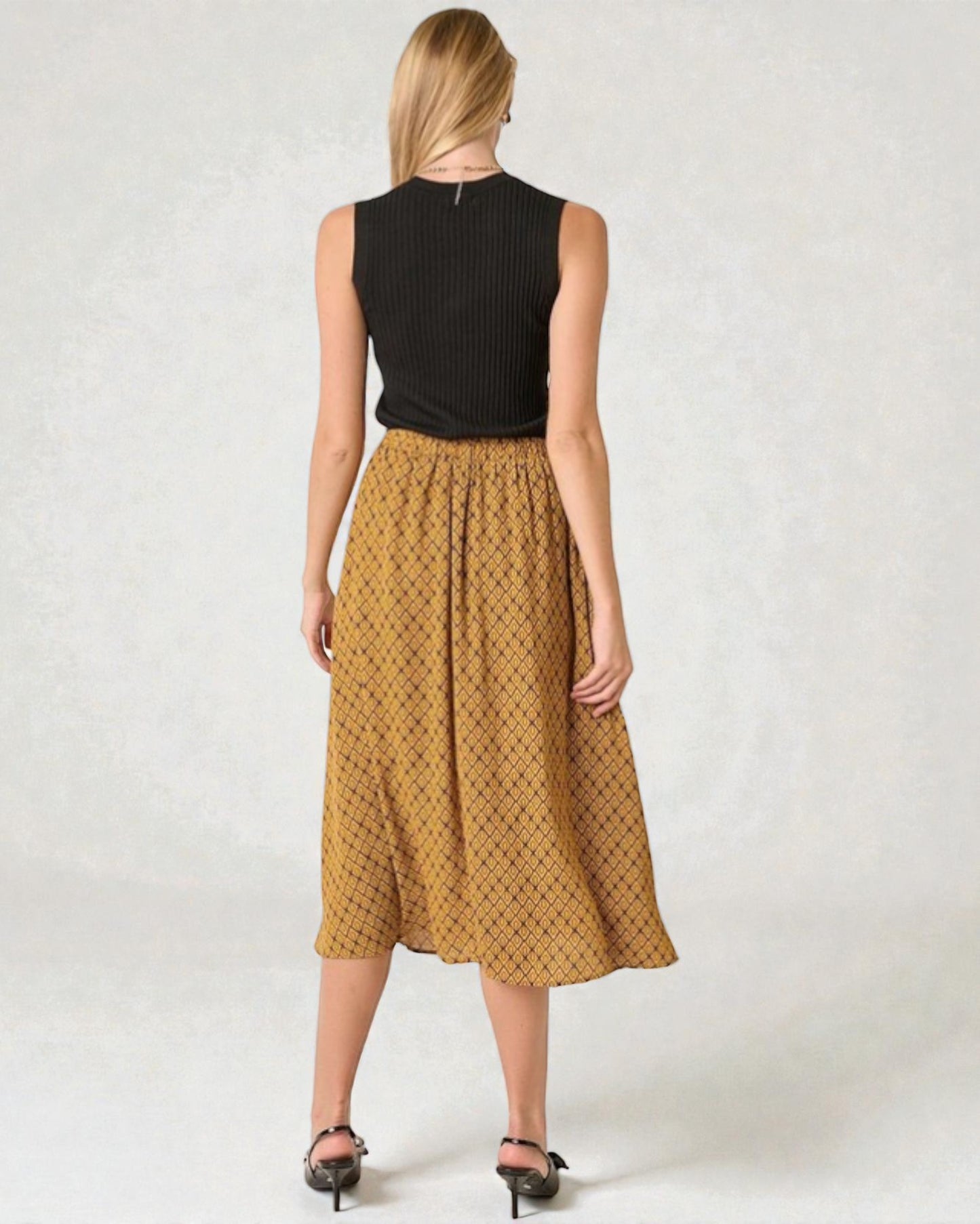 Woman wearing a black sleeveless top and mustard yellow patterned skirt on a white background
