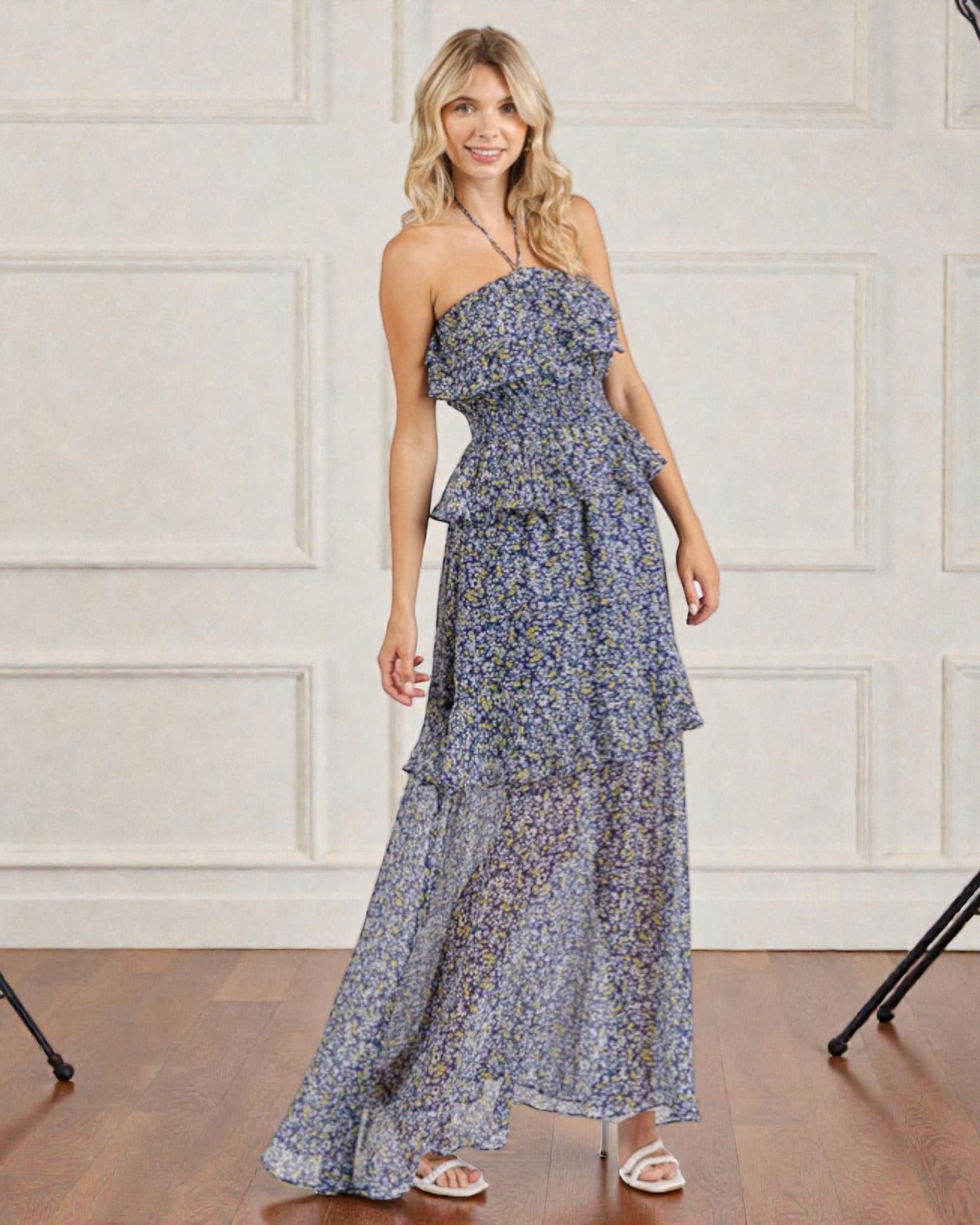 Woman wearing a floral one-shoulder dress against a white paneled wall.