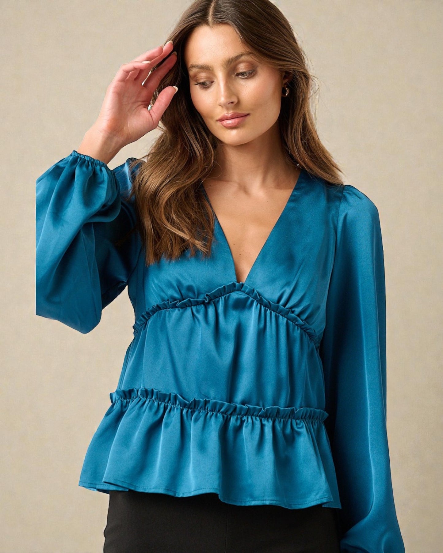 Woman wearing a blue blouse with long sleeves against a beige background