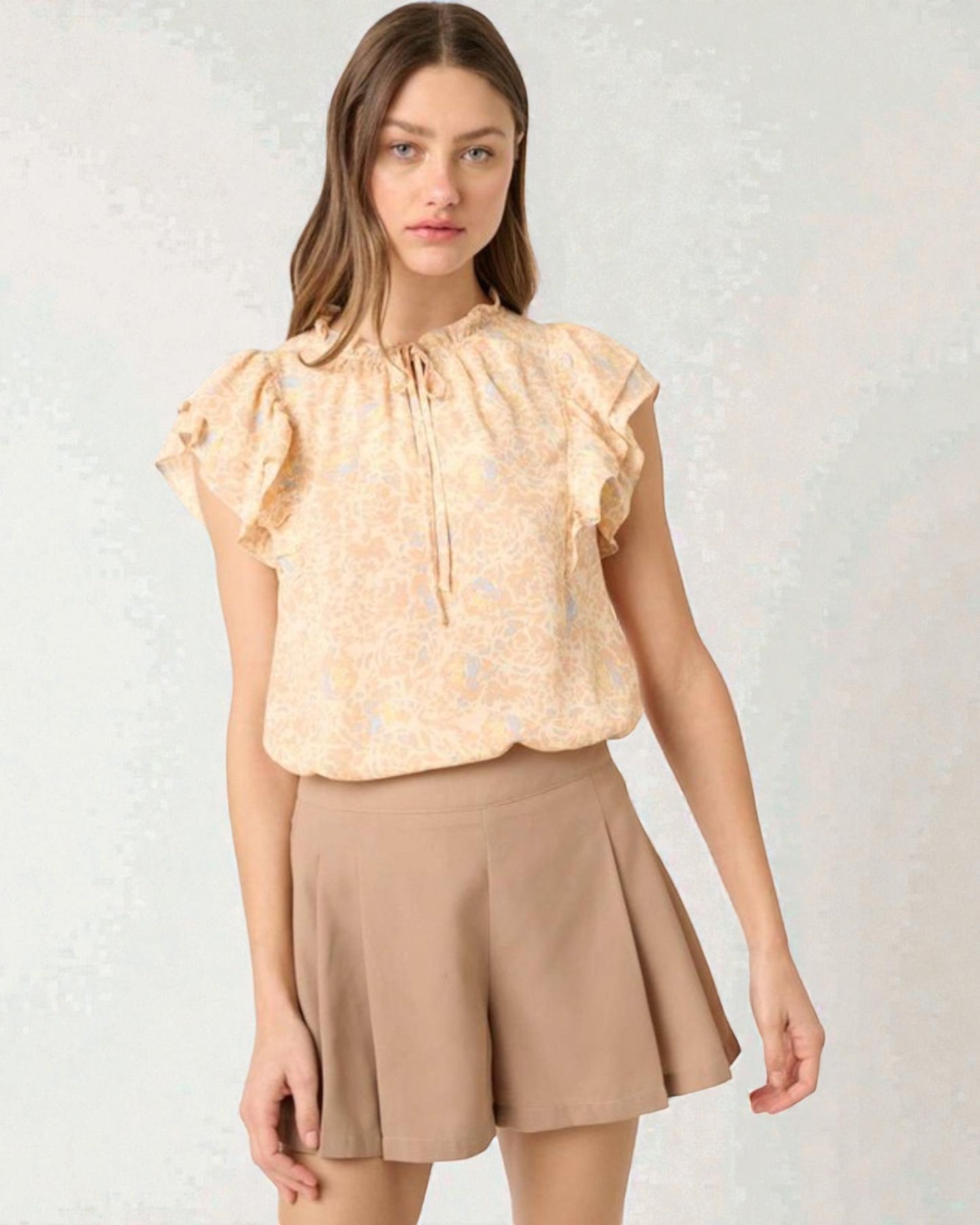 Woman wearing a beige blouse with ruffled sleeves and a matching skirt on a light background