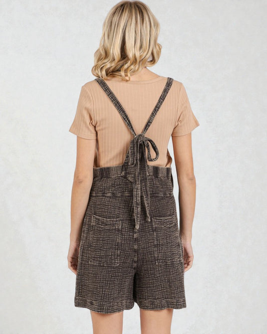 Person wearing a brown checkered dress with suspenders on a white background