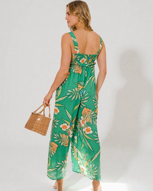 Woman wearing a green floral jumpsuit holding a woven bag against a white background