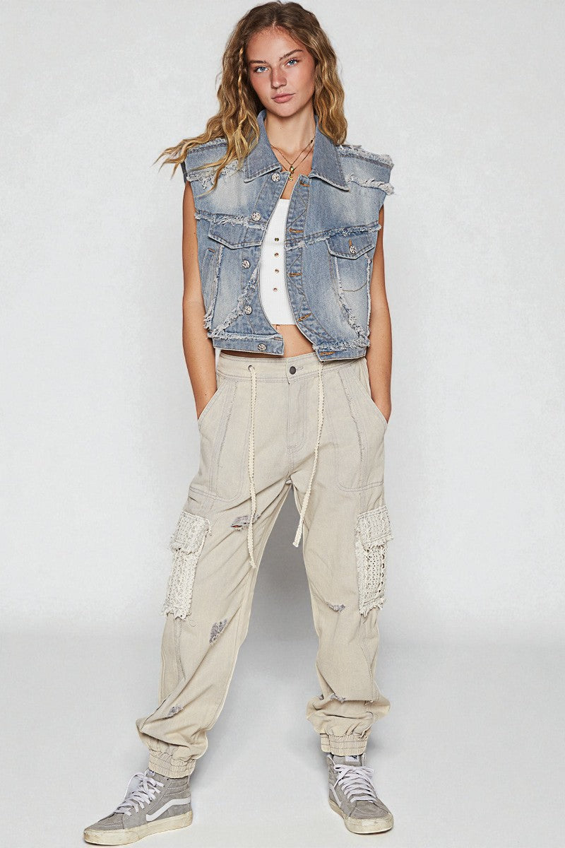 Woman wearing a denim vest, white top, beige cargo pants, and gray sneakers on a white background