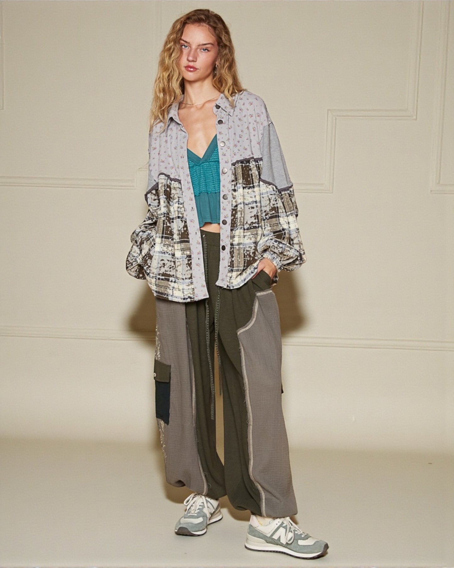 Woman wearing a plaid shirt, teal top, and gray pants against a plain background