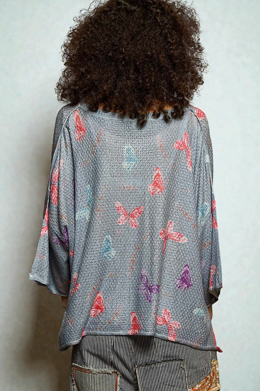 Person wearing a gray kimono-style garment with butterfly patterns on a plain background