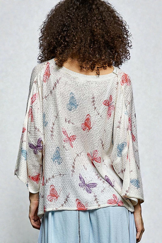 Person wearing a light-colored cardigan with butterfly pattern on a plain background