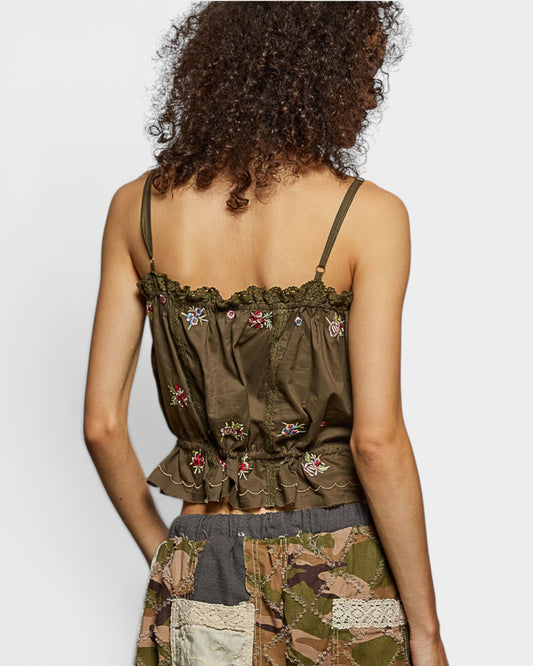 Person wearing a green embroidered top with floral patterns on a plain background