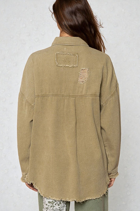 Person wearing a beige distressed denim jacket against a white background