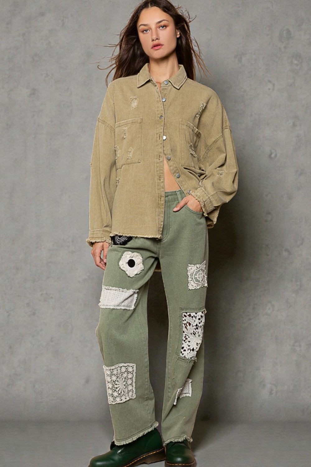 Woman wearing a beige jacket and green patchwork pants against a gray background