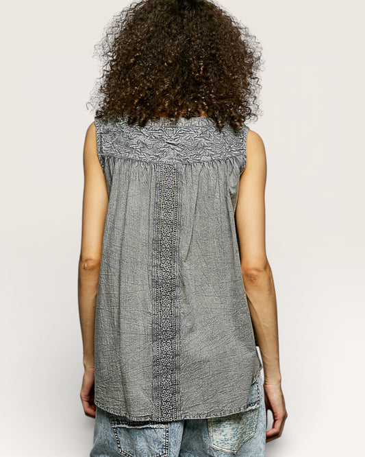 Person wearing a sleeveless patterned top against a plain background