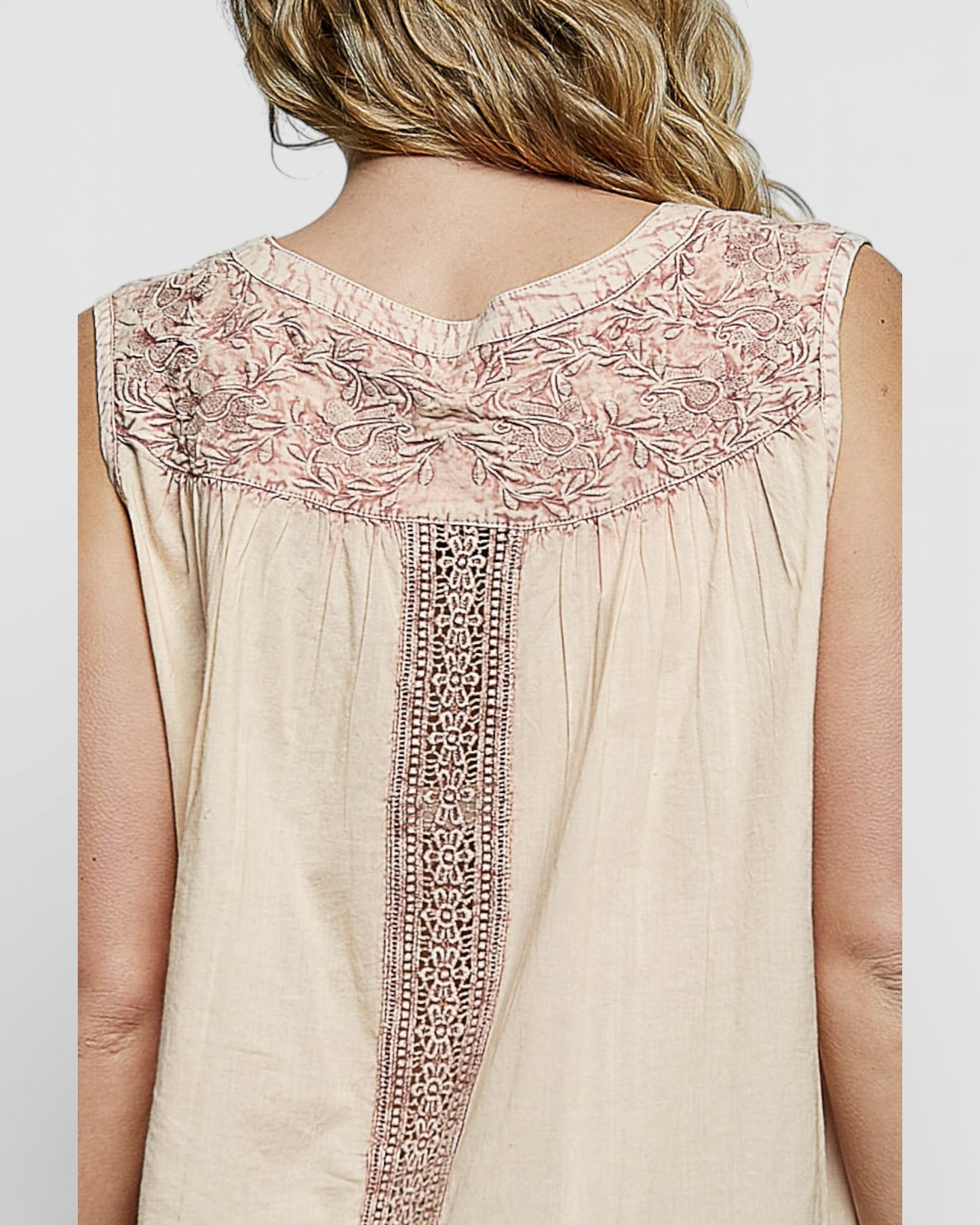 Beige sleeveless top with intricate pink embroidery on a plain background