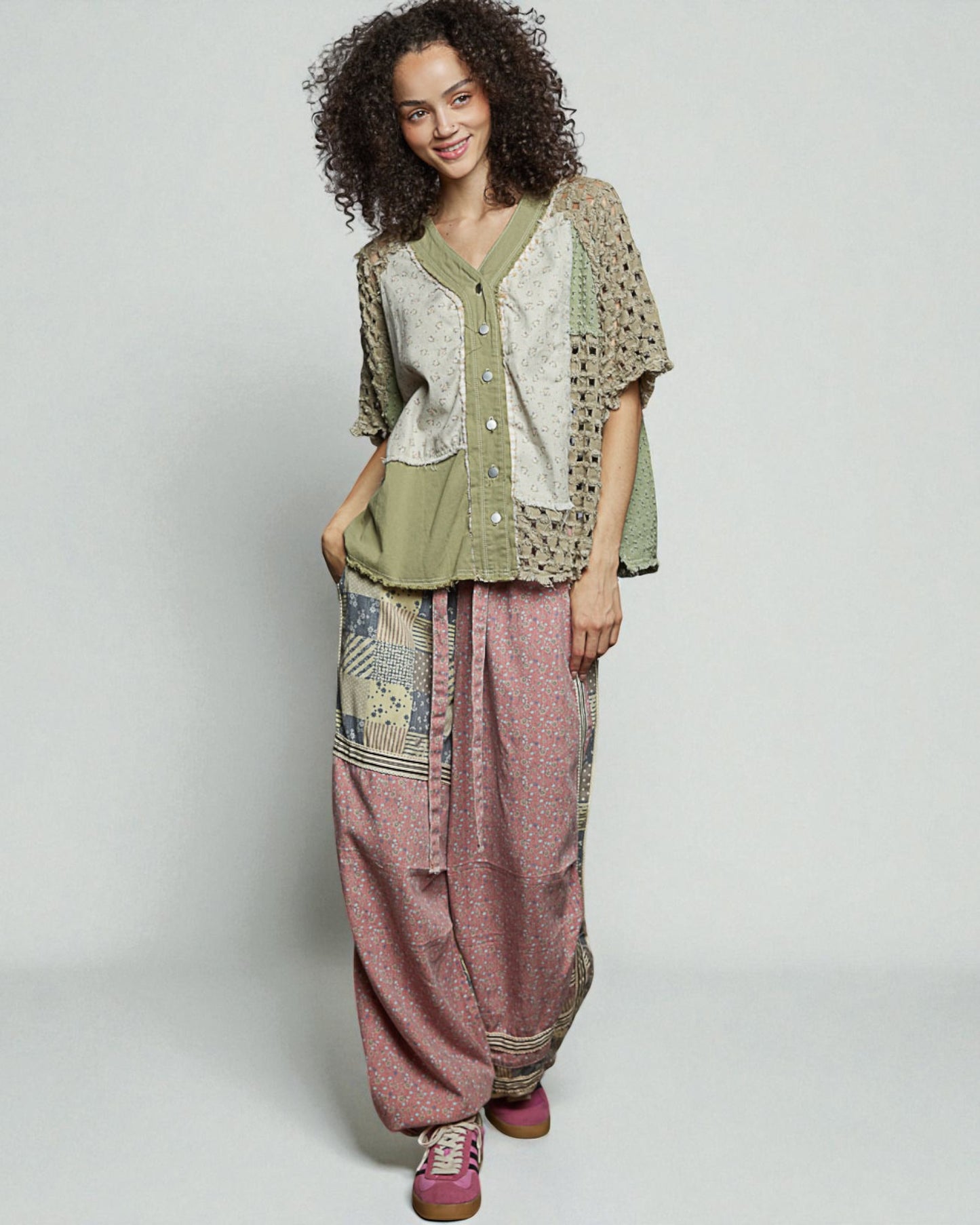 Woman wearing a green top and pink pants with a patterned jacket on a white background