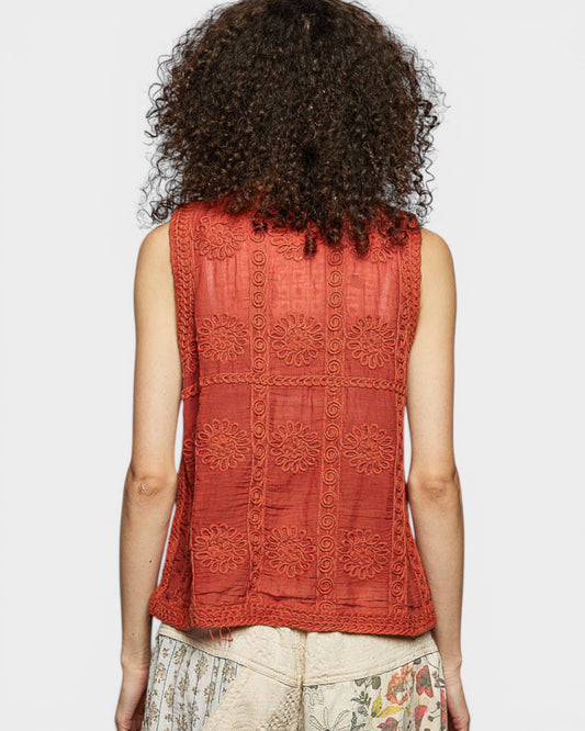 Person wearing a red sleeveless top with intricate patterns on a plain background