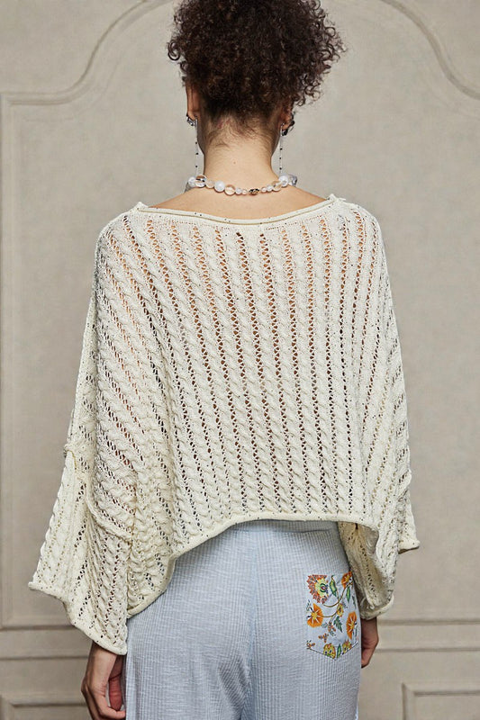 Person wearing a light-colored knit poncho with a neutral background