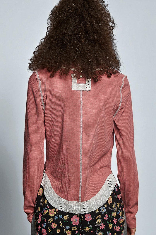 Person wearing a pink textured top with lace details and floral skirt on a plain background