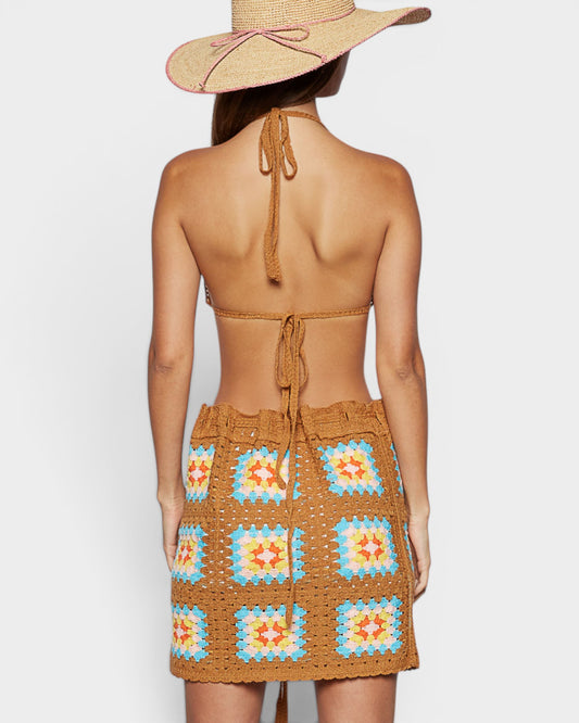 Woman wearing a brown crochet dress with colorful patterns and a wide-brimmed hat on a white background