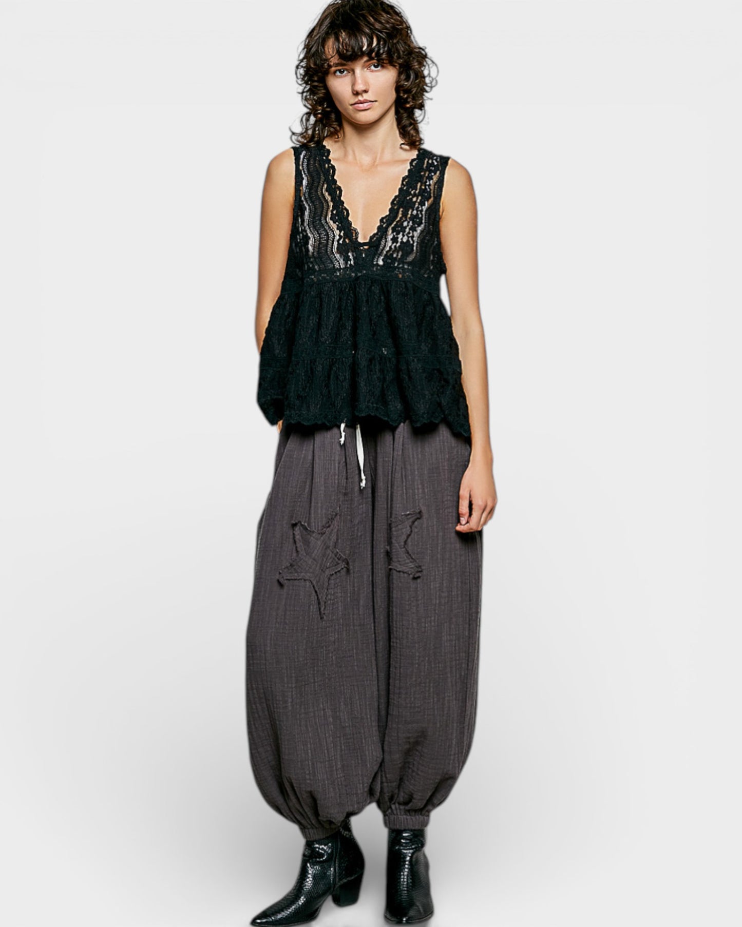 Woman wearing a black lace top and gray harem pants on a white background