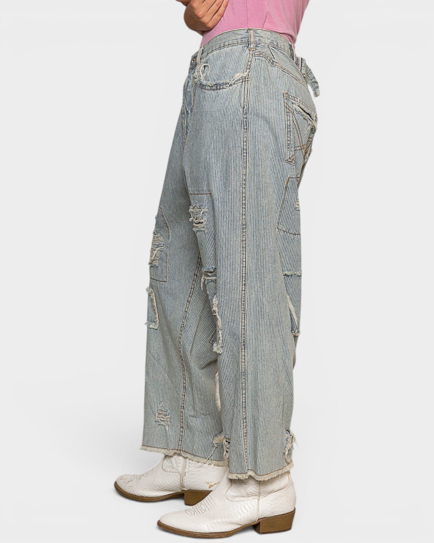 Person wearing light blue distressed jeans and white boots on a plain background